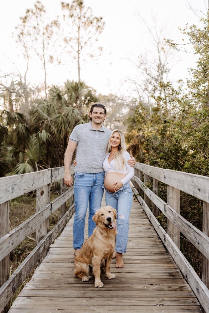 Couple embracing during their maternity session with their golden retriever during their maternity session in holiday florida