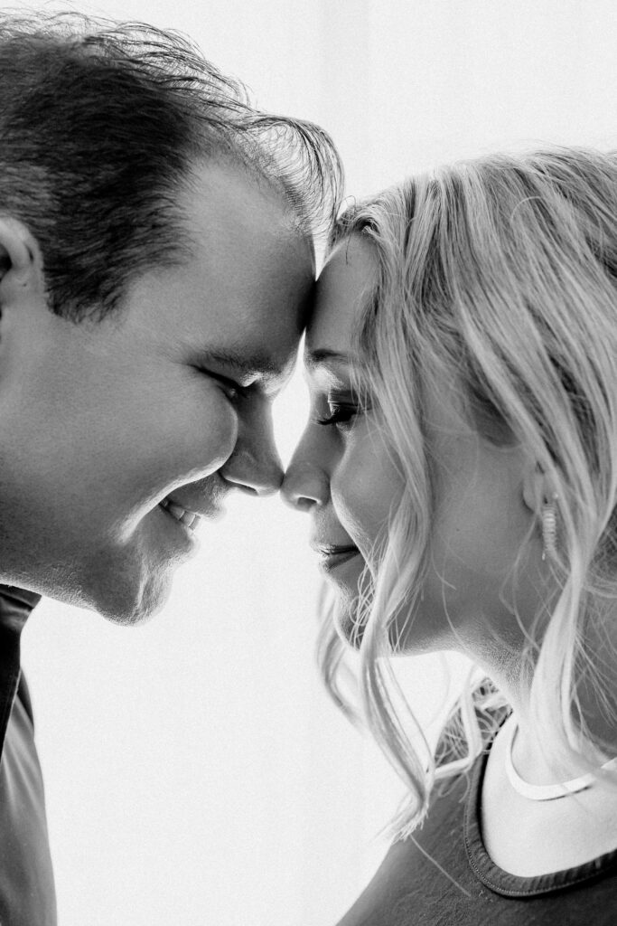 Close-up black and white photo of expectant couple touching foreheads and smiling softly during intimate maternity shoot