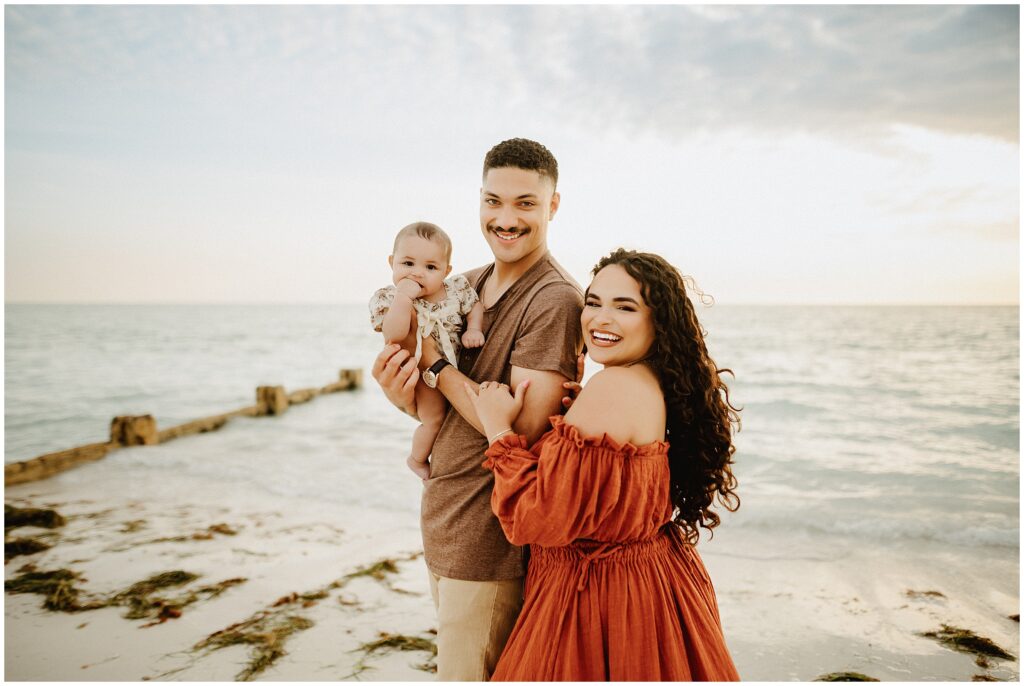 Happy man in a brown shirt and khaki pants enjoying a family moment with his wife and child on Honeymoon Island beach.