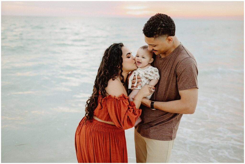 Beautiful family portrait on Honeymoon Island beach, featuring Taylor in a rust-colored two-piece dress, her husband in a brown shirt and khaki pants, and their adorable child