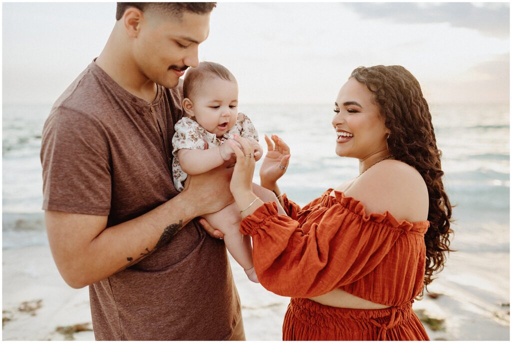 Scenic family portrait on Honeymoon Island beach, featuring Taylor, her husband, and their child against a backdrop of ocean waves and cloudy skies