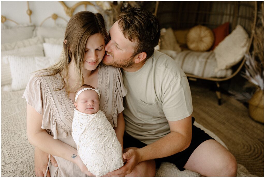 Heartwarming family portrait featuring mom Julie in a stunning neutral beige dress and dad in a pale green t-shirt, with their newborn baby girl in a boho-inspired studio