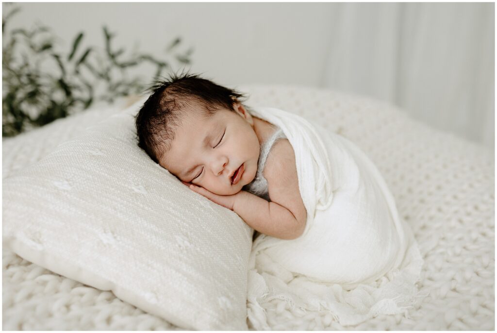 Posed newborn photo of baby boy with dark hair on white pillow in Springhill Florida studio