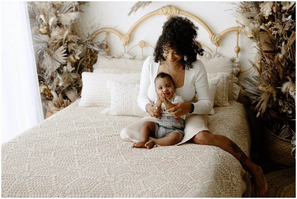 Smiling mom and son playing on a bed in a session at springhill florida photography studio