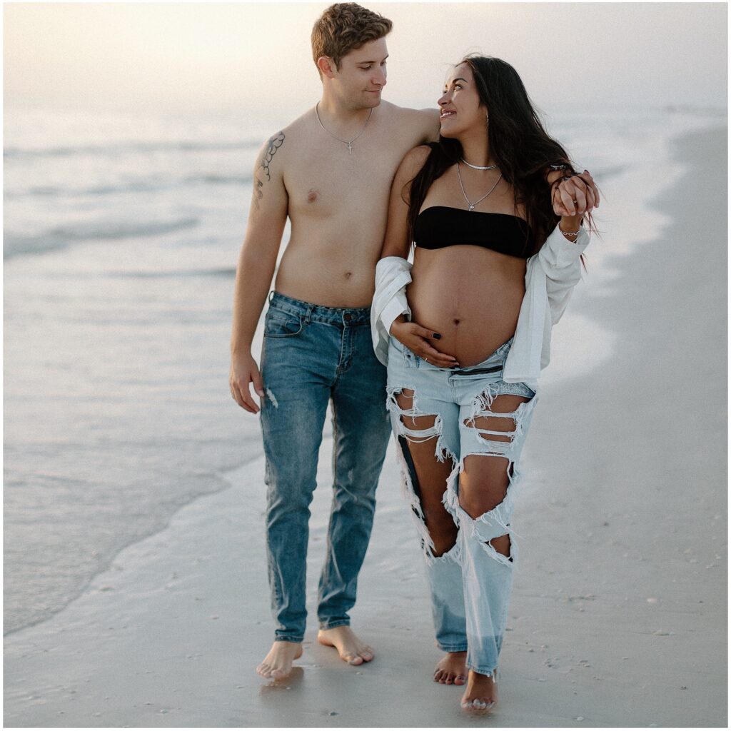 Maternity portraits of mom and dad holding hands while at beach in water in springhill florida