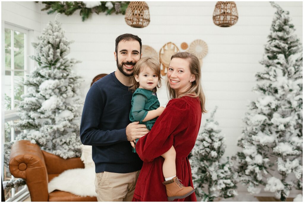 Mom in red dress, dad in blue sweater, and daughter in green dress with boots at Winter Wonderland Cottage in Tampa