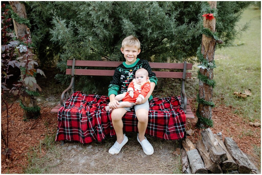 Baby girl in big brother's arms on bench with holiday blanket at Blue Acres Christmas Tree Farm in Tampa