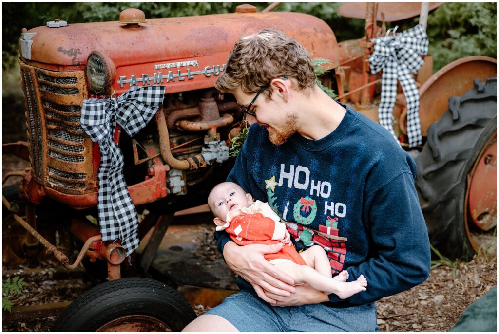 Baby girl in dad's arms by tractor at Blue Acres Christmas Tree Farm in Tampa