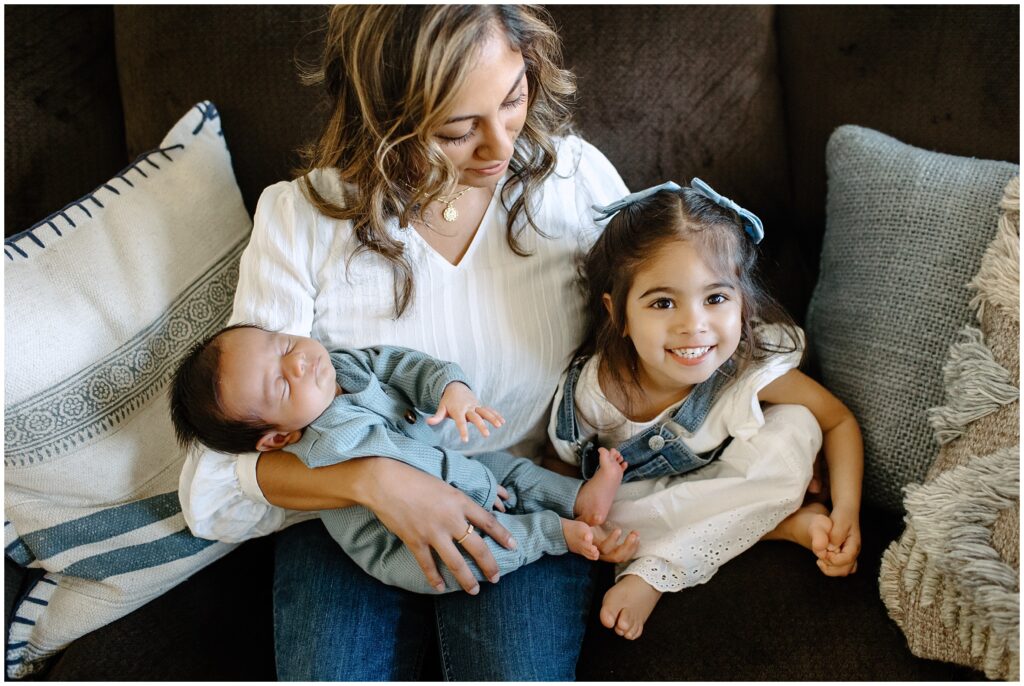 Mom and daughter with newborn brother laughing together on the couch