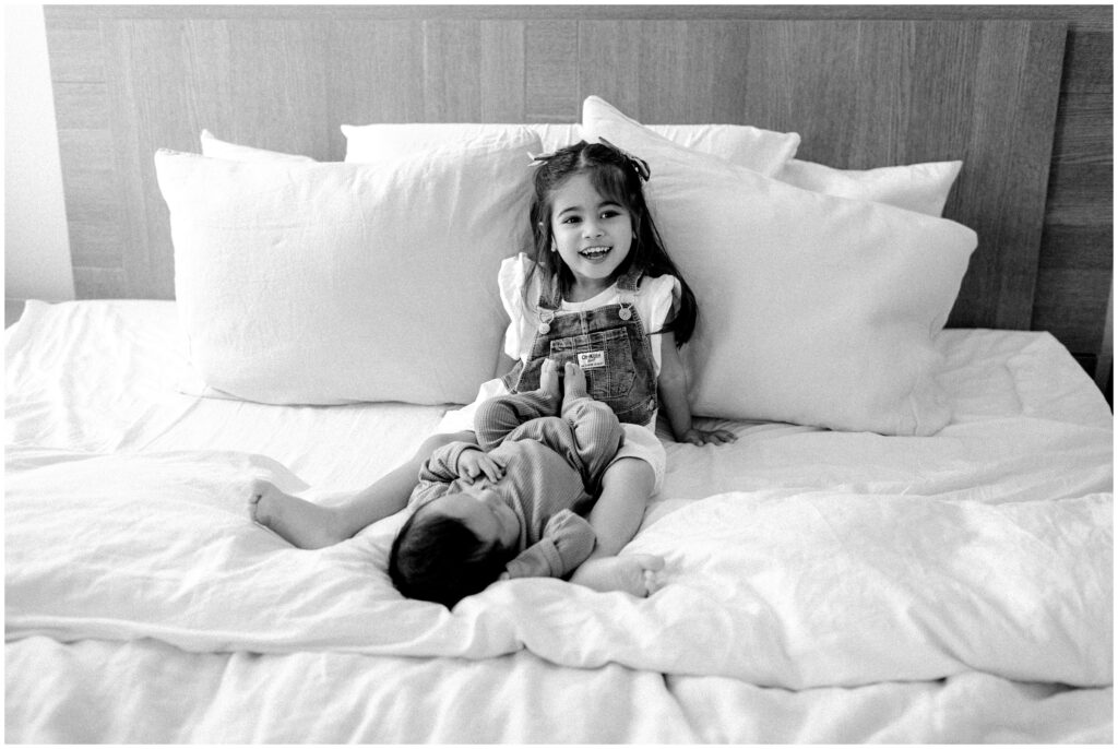 Black and white portrait of newborn baby boy and big sister on bed laying 