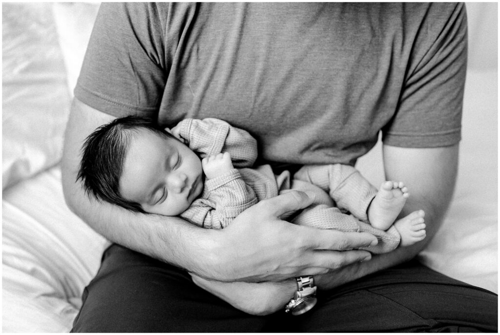 Close up black and white image of newborn baby boy sleeping in dad's arms