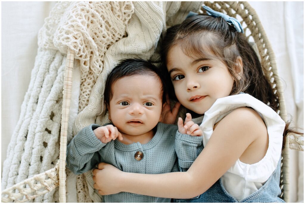 Newborn baby cuddling with big sister on bed in basket during newborn lifestyle