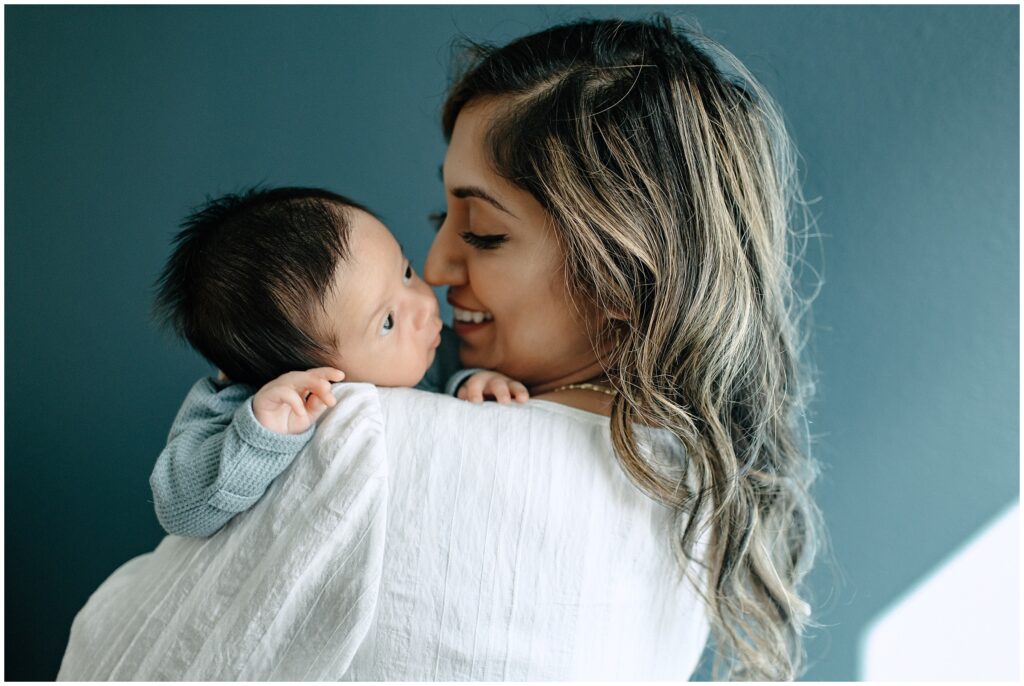 Close up portraits of mom smiling at newborn baby boy in front of blue wall