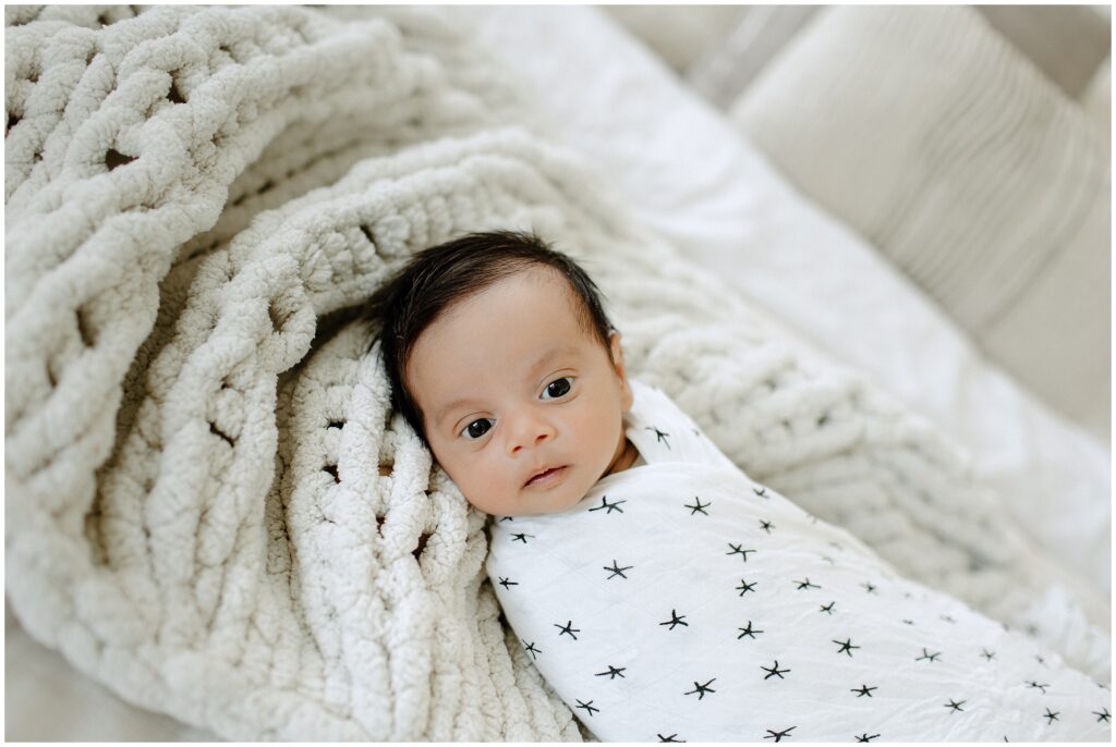 Newborn baby boy wrapped swaddle laying on white knit blanket