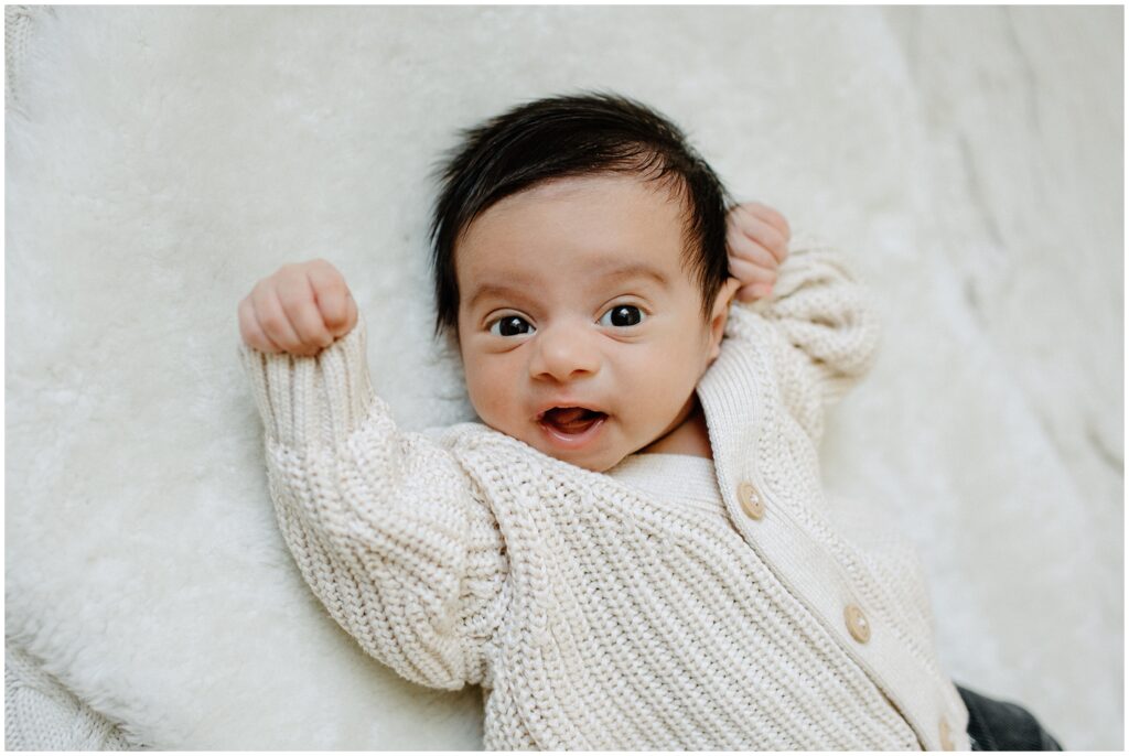 Newborn baby boy in knit sweater with hand up and eyes open during photo session