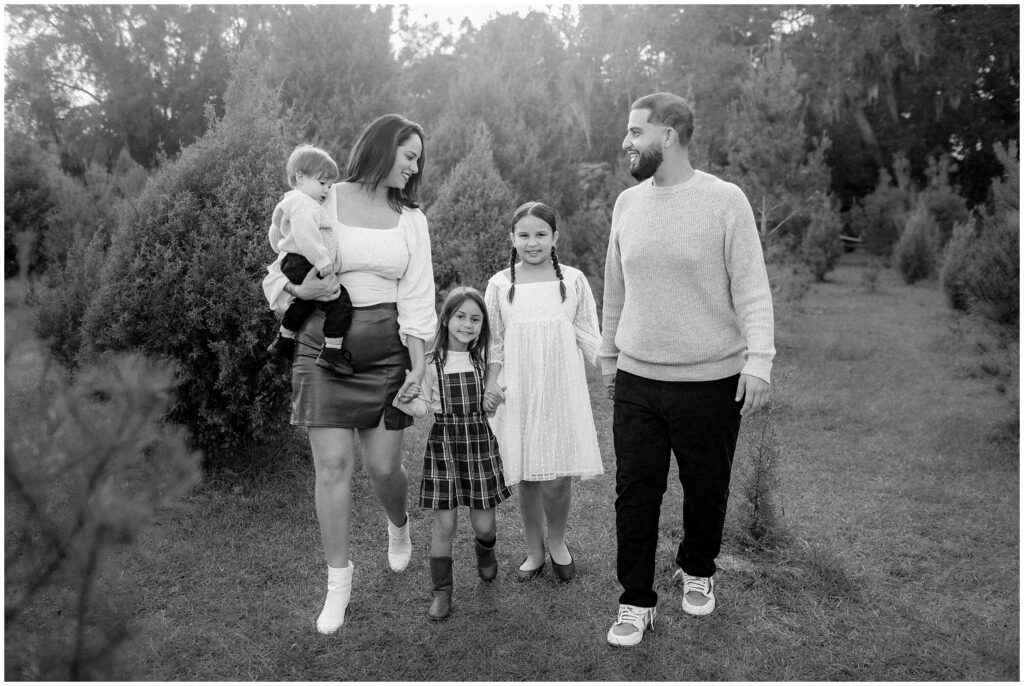 Black and white photo of family of 5 looking at each other and walking during session at Blue Acres Christmas Tree Farm in Florida