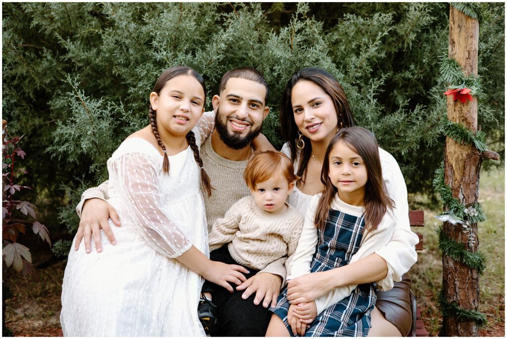 Family of 5 sitting on bench during holiday session at Blue Acres Christmas Tree Farm in Florida