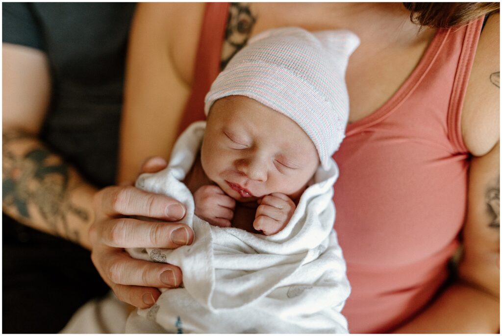 Newborn baby sleeping in mom's arms while swaddled with dad's hand fresh 48 hospital newborn session in Florida