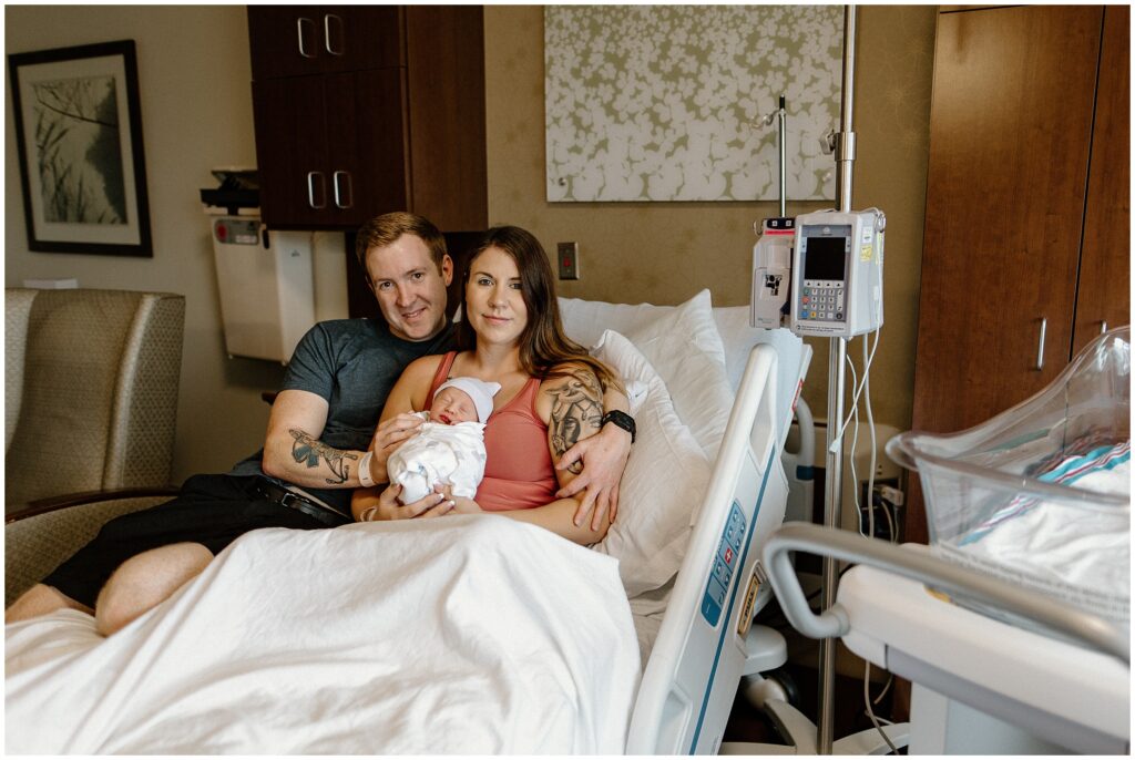 Mom and dad in hospital bed while mom holds newborn baby fresh 48 hospital newborn session in Florida