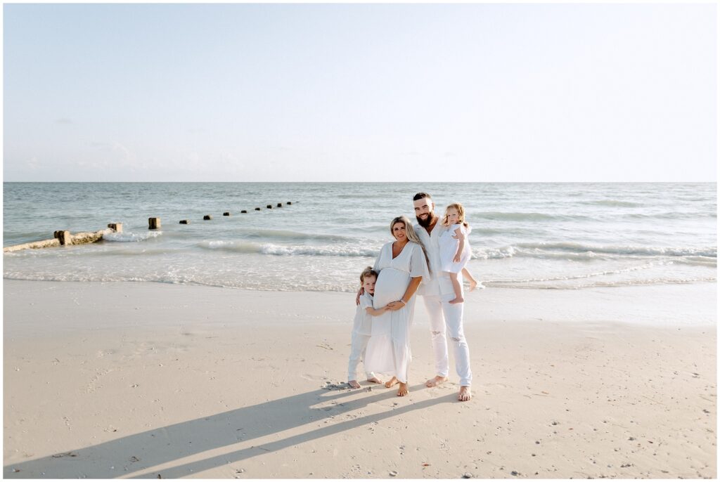 Mom, dad, little girl, and little boy in white outfits at a beach maternity session in Tampa