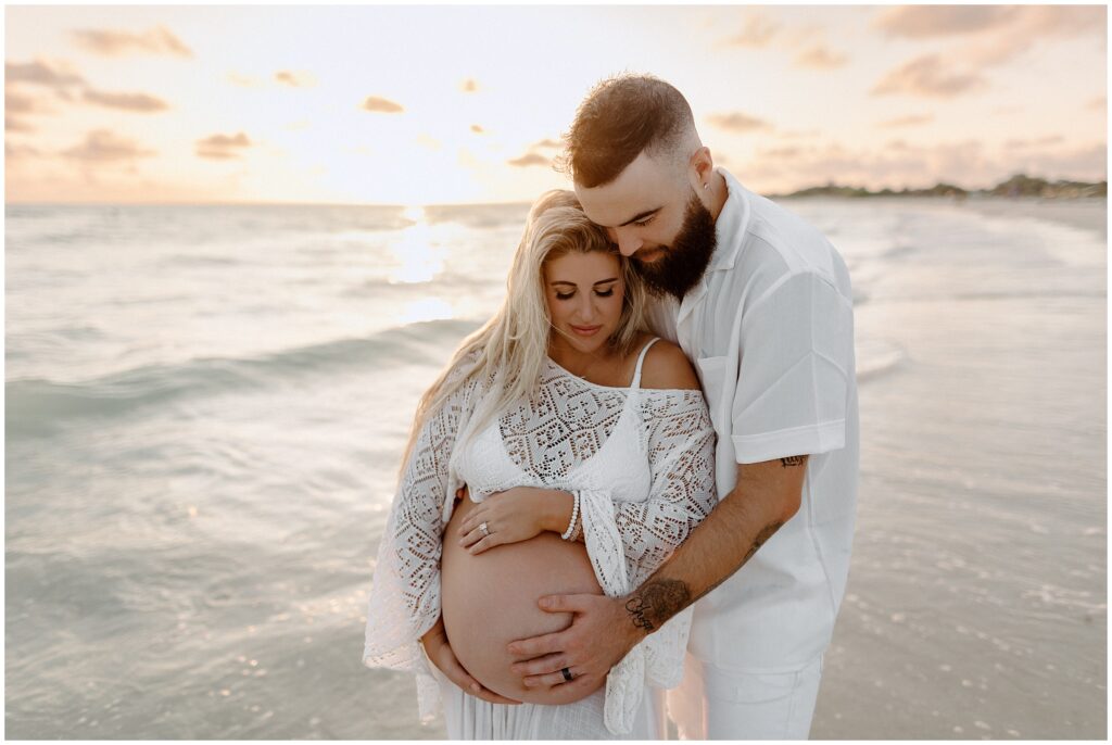 Close up portrait of mom in white two piece outfit and dad holding belly during sunset in Tampa on beach