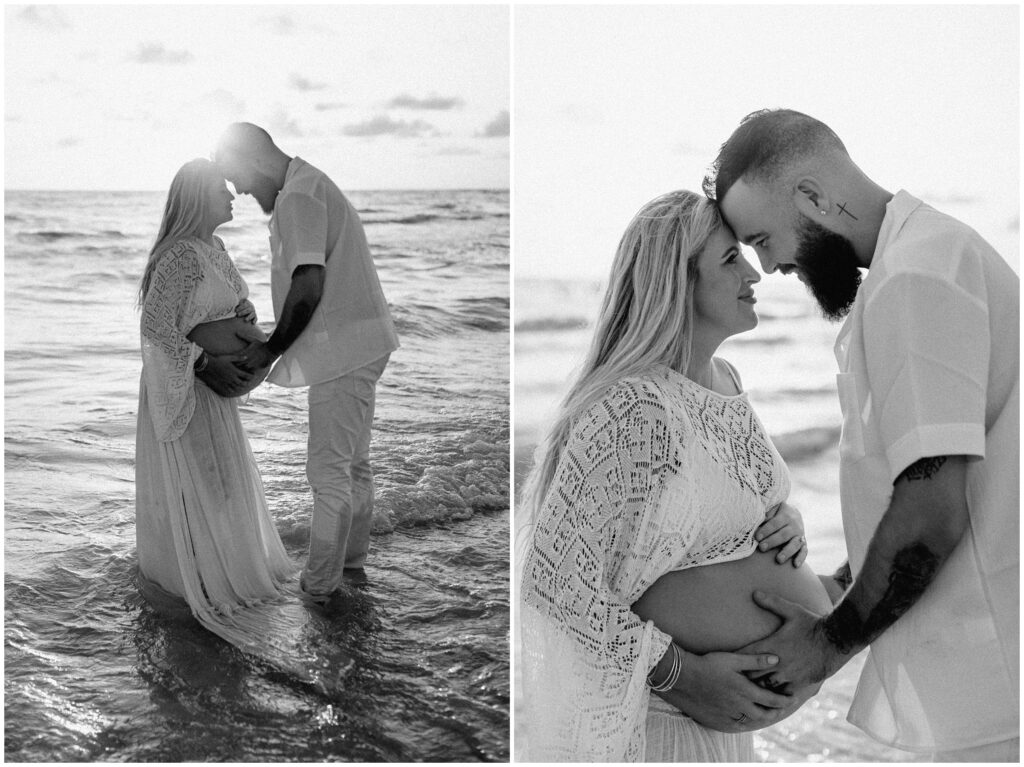 Black and white portraits of mom and dad with heads together in water holding belly in Tampa at beach