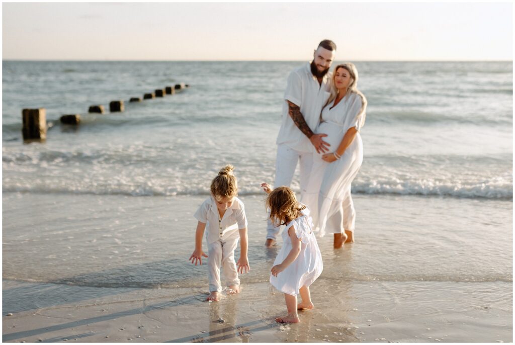 Maternity session of kids and parents playing in sand and water at beach in Tampa 