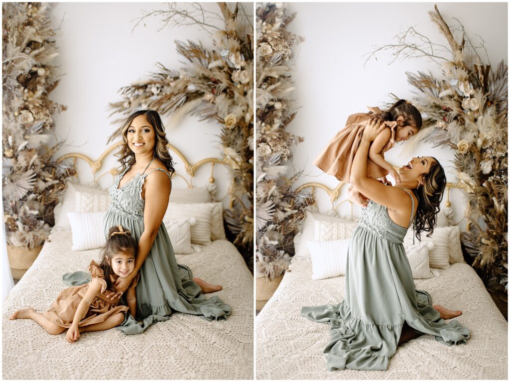 Pregnant woman in green dress playing with daughter on bed at Vibe Studio Spring Hill in Florida with boho vibes 