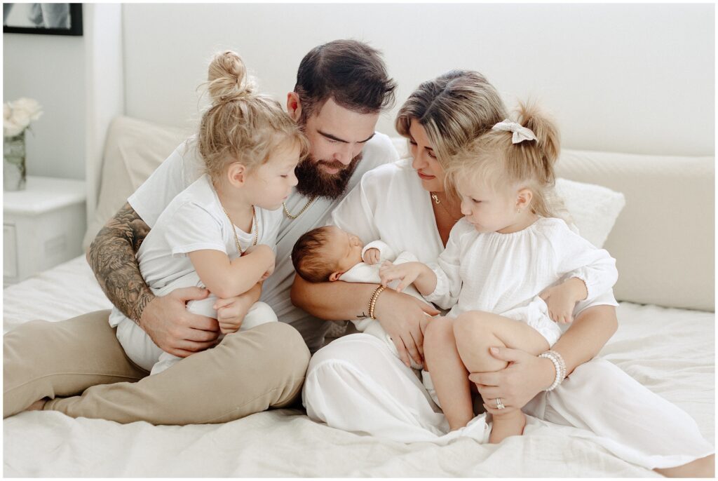 Family of 5 sitting on bed cuddling in home newborn lifestyle photo session in Florida