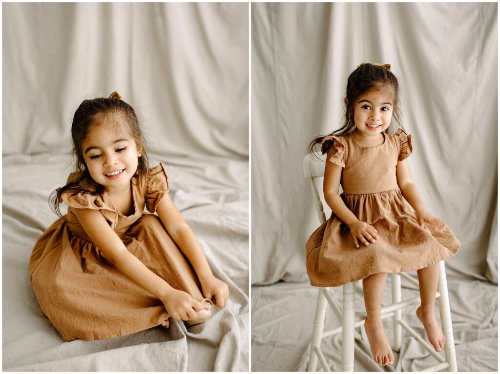 Little girl in rust color dress sitting and smiling in front of beige fabric at Vibe Studio Spring Hill in Florida