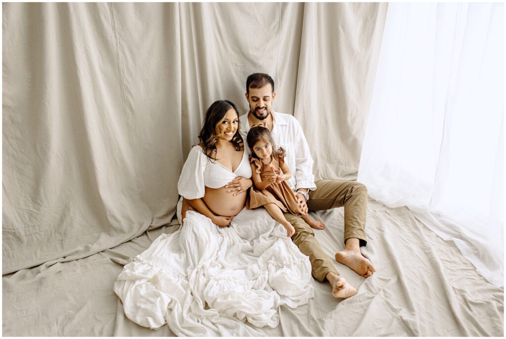 Mom, daughter, and dad sitting on beige fabric at Vibe Studio Spring Hill in Florida