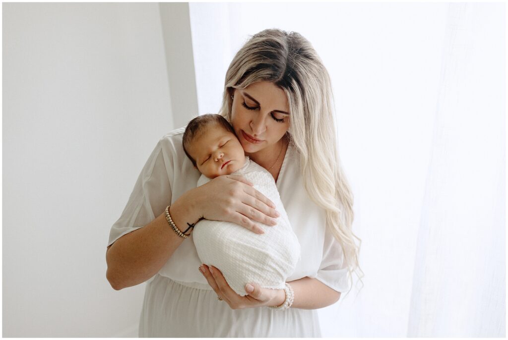 Mom holding swaddled newborn baby boy in home newborn lifestyle photo session in Florida