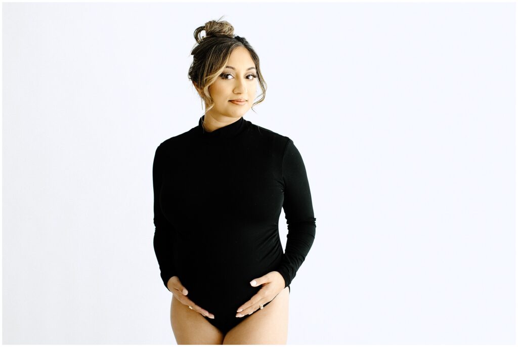 Pregnant woman with hair up wearing black long sleeve bodysuit in front of white backdrop at Vibe Studio Spring Hill in Florida