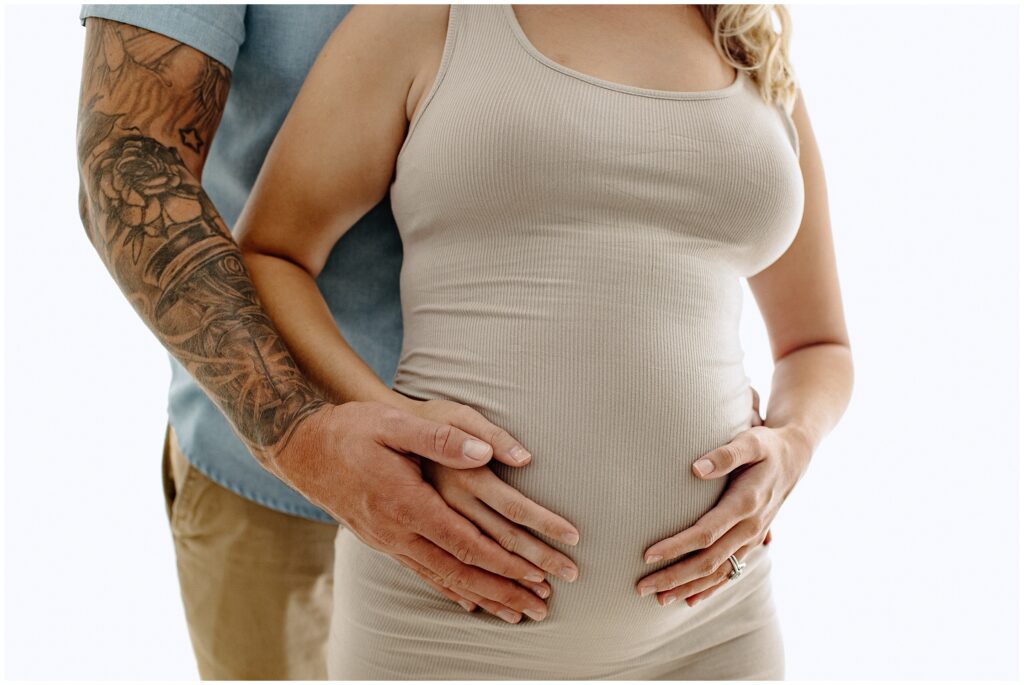 Close up portrait of pregnant woman in a nude dress with her partner holding belly at Spring Hill Studio.