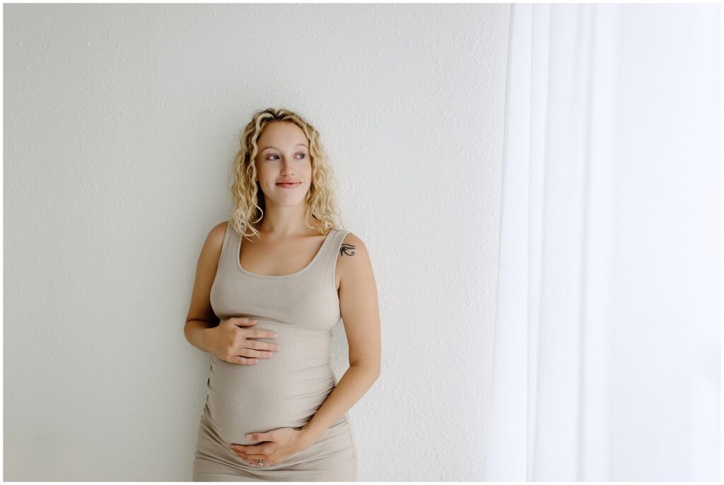 Close up portrait of pregnant woman in nude dress holding stomach during maternity session 