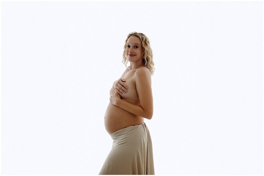 Maternity session with pregnant woman in nude fabric skirt, topless, holding belly at Spring Hill Studio in Florida