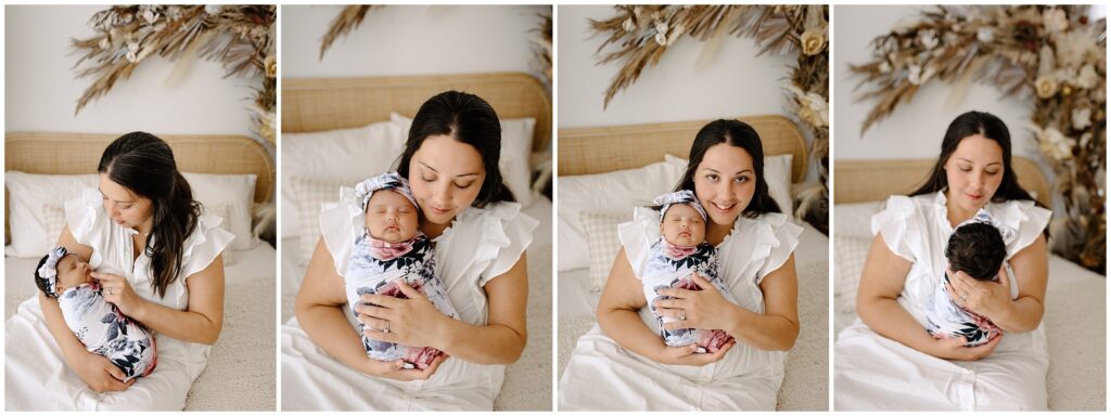 Mom sitting on bed in white dress holding newborn baby girl in floral swaddle newborn session at Spring Hill Studio in Florida